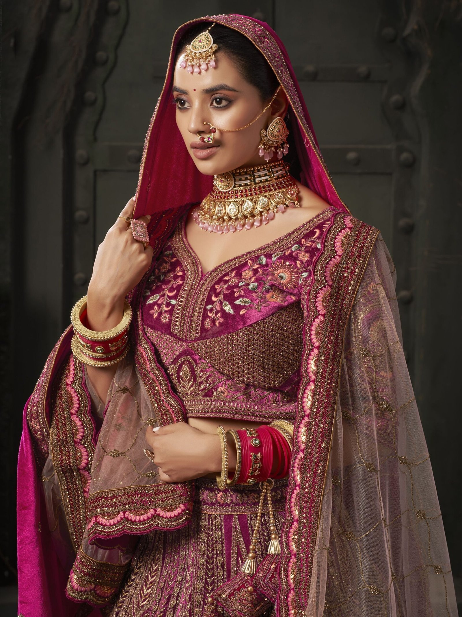 Indulge in the regal allure of this magnificent maroon color velvet bridal lehenga, meticulously crafted to adorn the bride in timeless elegance and sophistication. Luxuriously crafted from sumptuous velvet material, this ensemble is adorned with a mesmerizing array of embellishments, including multi-thread work, sequin work, diamond work, zari work, velvet embroidered patchwork, and fancy dori work, ensuring a breathtakingly opulent aesthetic. Accompanying the lehenga is a matching velvet choli, intricately detailed with similar multi-thread work, sequin work, diamond work, zari work, embroidered work, and fancy dori work, creating a harmonious and refined ensemble. The semi-stitched design of the lehenga offers a comfortable fit of up to 42 inches, allowing for ease of movement and flexibility. Additionally, the un-stitched choli material provides the opportunity for customization, ensuring a tailored and flattering silhouette for the bride. Completing the ensemble are two double dupattas crafted from similar maroon net and velvet material, adorned with exquisite lace work and butta work on all four sides. These dupattas add an ethereal touch of romance and grace, draping gracefully over the shoulders and enhancing the overall beauty of the bridal look. Whether worn traditionally or styled in a modern manner, these dupattas add a layer of sophistication and glamour to the ensemble. Draping yourself in this featured maroon color velvet bridal lehenga is not merely about wearing a garment; it's about embodying a sense of timeless beauty and refinement. Each element of this ensemble has been thoughtfully curated to ensure that the bride radiates confidence and grace on her special day. Prepare to receive an abundance of compliments as you showcase your impeccable taste and sophisticated style with this breathtaking bridal lehenga, destined to make you the epitome of elegance and grace on your wedding day. Disclaimer: Slight color variation may occur due to photographic reasons. - Image 2