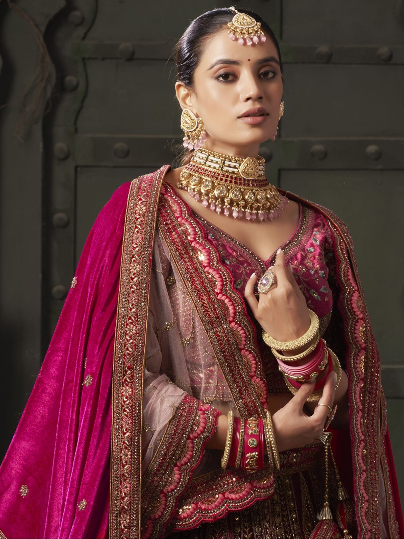 Indulge in the regal allure of this magnificent maroon color velvet bridal lehenga, meticulously crafted to adorn the bride in timeless elegance and sophistication. Luxuriously crafted from sumptuous velvet material, this ensemble is adorned with a mesmerizing array of embellishments, including multi-thread work, sequin work, diamond work, zari work, velvet embroidered patchwork, and fancy dori work, ensuring a breathtakingly opulent aesthetic. Accompanying the lehenga is a matching velvet choli, intricately detailed with similar multi-thread work, sequin work, diamond work, zari work, embroidered work, and fancy dori work, creating a harmonious and refined ensemble. The semi-stitched design of the lehenga offers a comfortable fit of up to 42 inches, allowing for ease of movement and flexibility. Additionally, the un-stitched choli material provides the opportunity for customization, ensuring a tailored and flattering silhouette for the bride. Completing the ensemble are two double dupattas crafted from similar maroon net and velvet material, adorned with exquisite lace work and butta work on all four sides. These dupattas add an ethereal touch of romance and grace, draping gracefully over the shoulders and enhancing the overall beauty of the bridal look. Whether worn traditionally or styled in a modern manner, these dupattas add a layer of sophistication and glamour to the ensemble. Draping yourself in this featured maroon color velvet bridal lehenga is not merely about wearing a garment; it's about embodying a sense of timeless beauty and refinement. Each element of this ensemble has been thoughtfully curated to ensure that the bride radiates confidence and grace on her special day. Prepare to receive an abundance of compliments as you showcase your impeccable taste and sophisticated style with this breathtaking bridal lehenga, destined to make you the epitome of elegance and grace on your wedding day. Disclaimer: Slight color variation may occur due to photographic reasons. - Image 4